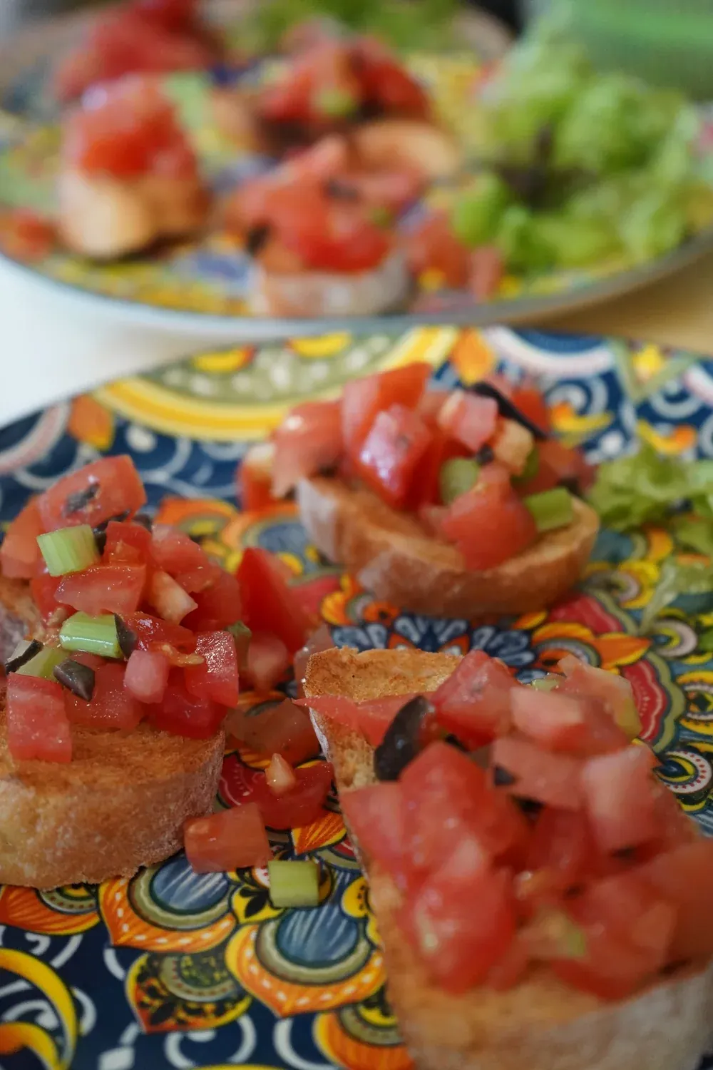 Bruschetta mit Tomatenwürfeln, Oliven und Frühlingszwiebeln auf einem bunt gemusterten Teller