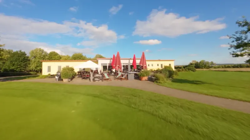 Die Terrasse des Restaurants Hole 19 mit roten Sonnenschirmen, dahinter das Clubhaus und der Golfplatz